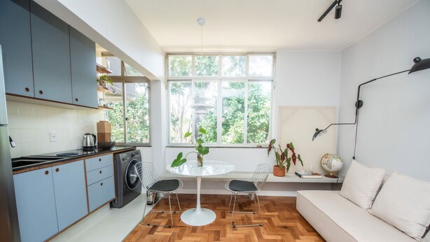 A modern kitchen with a built-in washing machine, a dining area with a round table and chairs, and a sofa. - Apto com Excelente Localiza o em Asa Sul DF (Brasília)