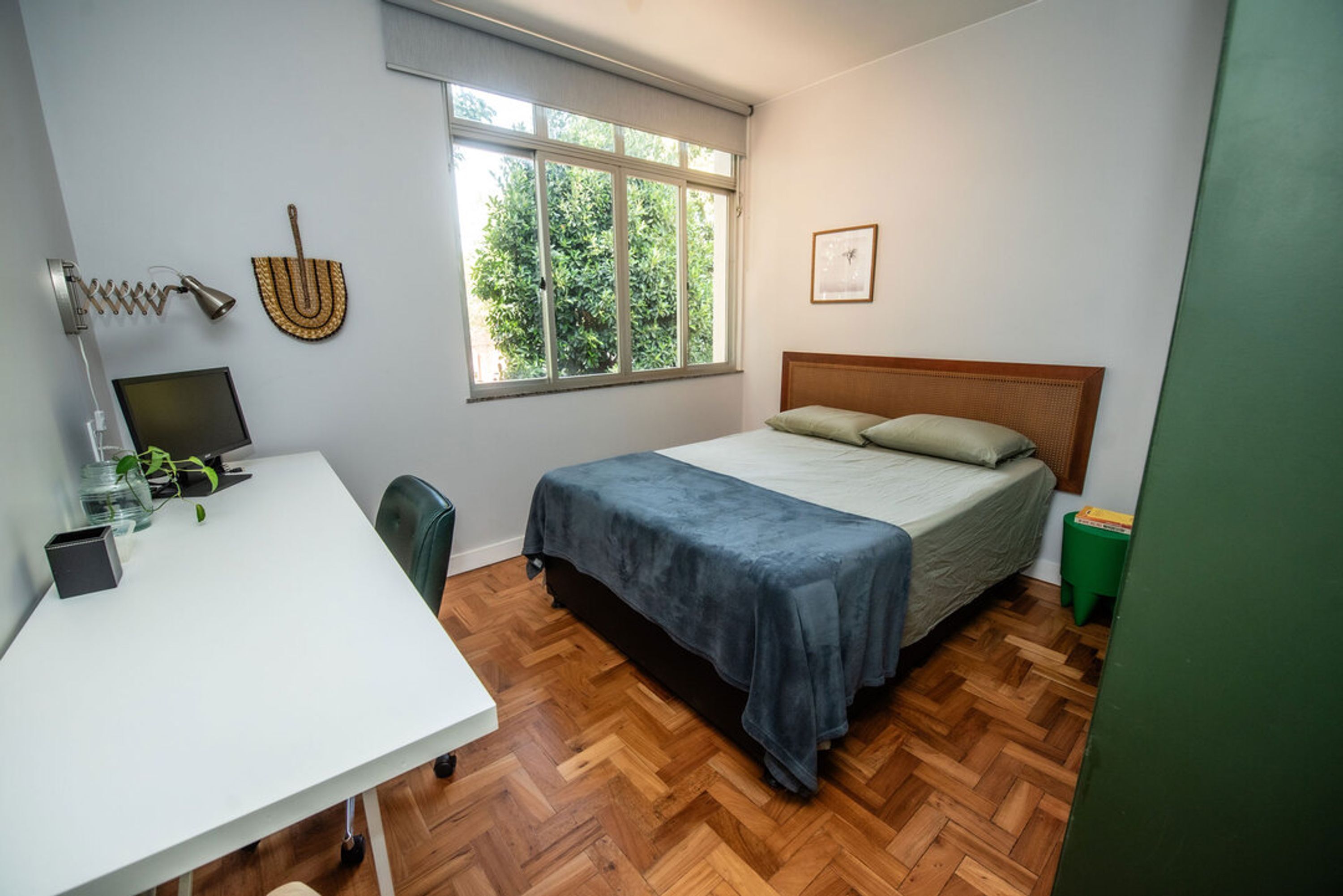 Ein Schlafzimmer mit einem Bett, einem Schreibtisch, einem Stuhl, einem Fenster und einem kleinen grünen Hocker.