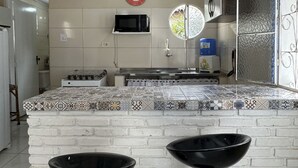 Ett kök med vita kakelplattor på väggen ovanför arbetsbänken, en mikrovågsugn, en spis och två svarta barstolar.