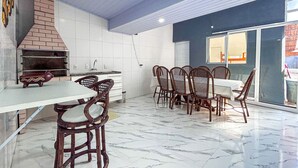 Μια κουζίνα με φούρνο από τούβλα, λευκά ντουλάπια και μια τραπεζαρία με ξύλινα καθίσματα και μαρμάρινο δάπεδο.
