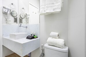 A bathroom with a sink, mirror, hairdryer, towel, and toilet. - Est dio com Wi-fi a 200m da Praia de Copacabana RJ (Rio de Janeiro)