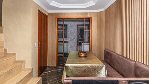 Corridoio che conduce a una sala da pranzo con un tavolo apparecchiato per due, una panca e una cucina visibile attraverso una porta in vetro.