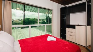 Una camera da letto con un'ampia finestra, un letto con coperta rossa e un armadio con diversi scomparti.