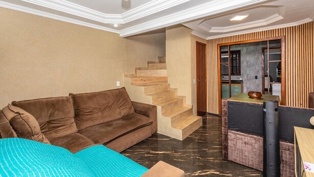 Un soggiorno con un divano marrone, una coperta color petrolio e una scala che conduce a una zona cucina.