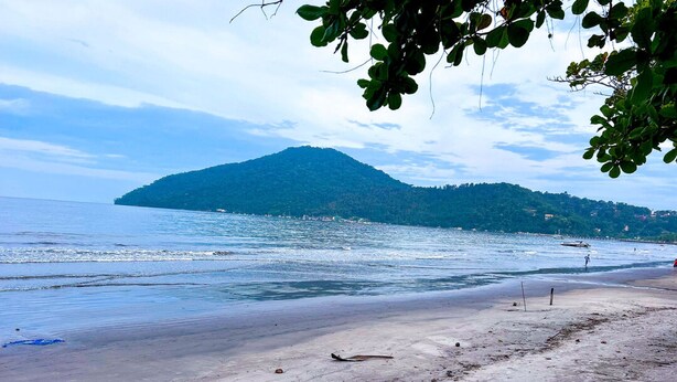 Ein Strand mit einem Berg im Hintergrund, ruhigem Wasser und blauem Himmel.