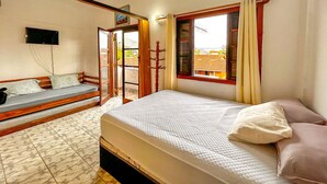 Ein Schlafzimmer mit einem Bett, einem Vorhangfenster, einem an der Wand montierten Fernseher und einer zur Außenseite führenden Tür.