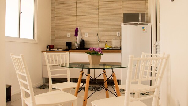 A compact kitchen with white cabinetry, a glass-top dining table, and white chairs.