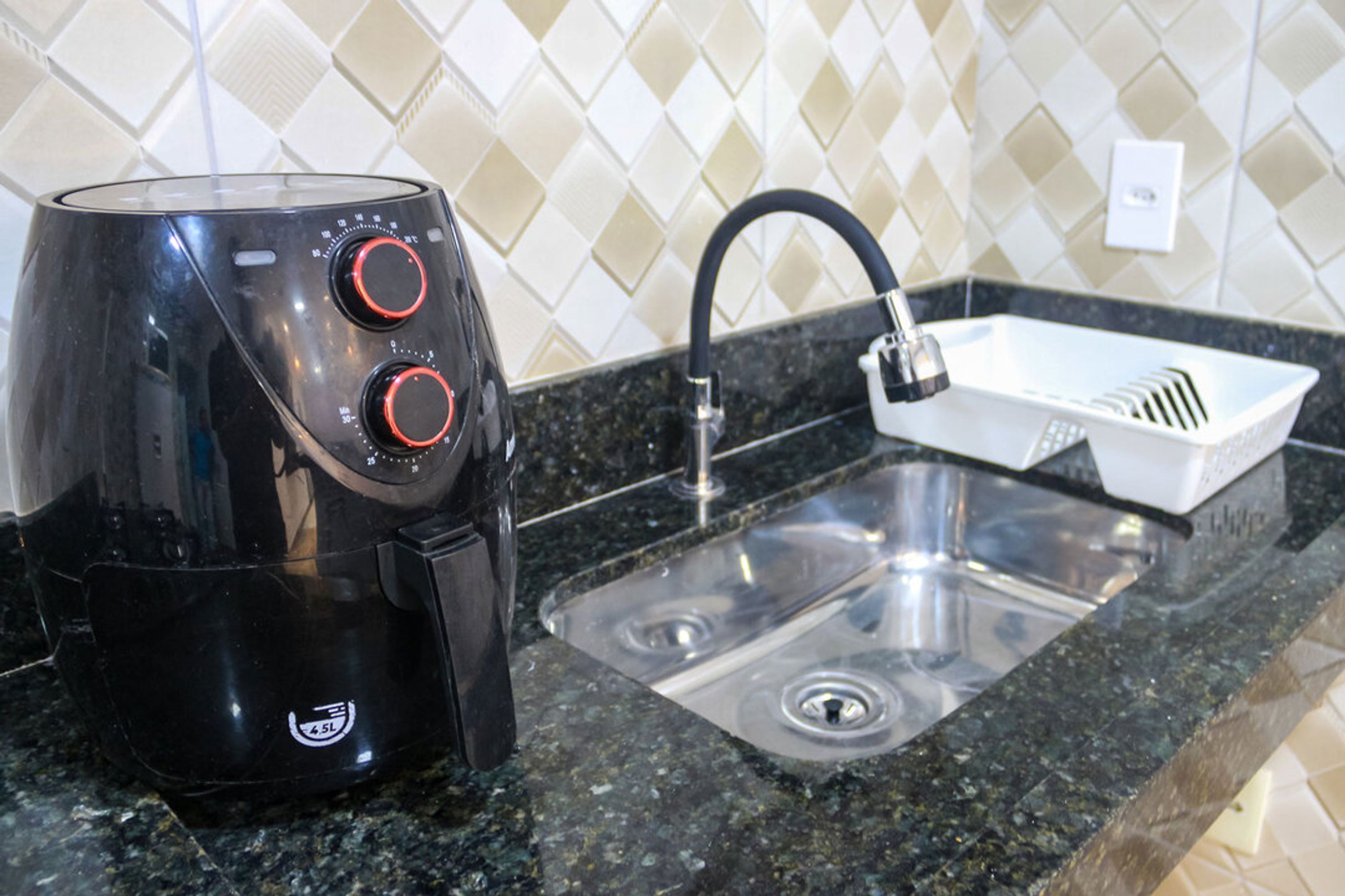Eine schwarze Kaffeemaschine mit zwei roten Drehknöpfen und einem weißen Behälter auf einer Arbeitsplatte aus Granit neben einem Edelstahl-Spülbecken.