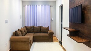 A modern living room with a brown sectional sofa, a white rug, a wooden TV stand, and a large window with curtains.