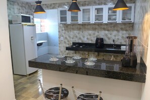A kitchen with a microwave, a coffee maker, and a blender on the counter. There are chairs and a window in the room. - Casa com Tima Localiza o em Porto Seguro BA (Porto Seguro)