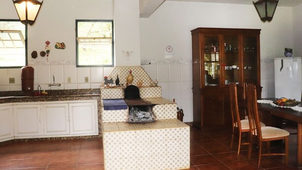 A kitchen with white cabinets, a checkered island, wooden chairs, and a cabinet with glass doors. - Lindo s tio com Piscina em Rio Novo-minas Gerais (Rio Novo)