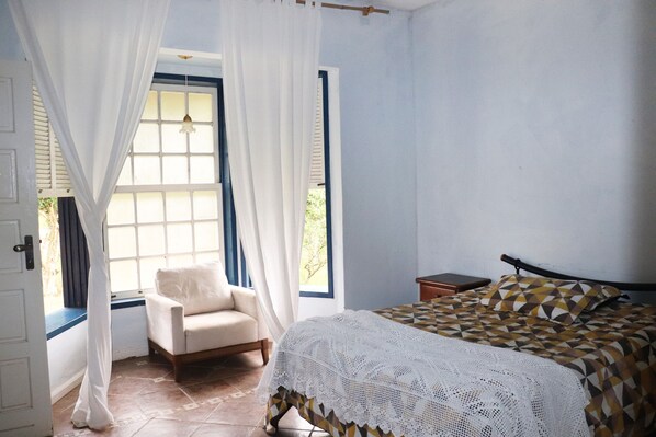 A bedroom with a bed, a chair, a window with curtains, and a bedside table. - Lindo s tio com Piscina em Rio Novo-minas Gerais (Rio Novo)