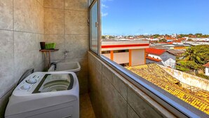 A bathroom with a washing machine, a sink, and a window with a city view. - Apto a 210m da Praia da Pontinha em Araruama RJ (Araruama)