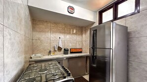 A kitchen with a stainless steel refrigerator, a gas stove, and a digital coffee maker. - Apto a 210m da Praia da Pontinha em Araruama RJ (Araruama)