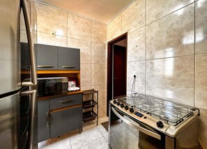 A compact kitchen with a built-in microwave, a gas stove, and a small refrigerator. - Apto a 210m da Praia da Pontinha em Araruama RJ (Araruama)