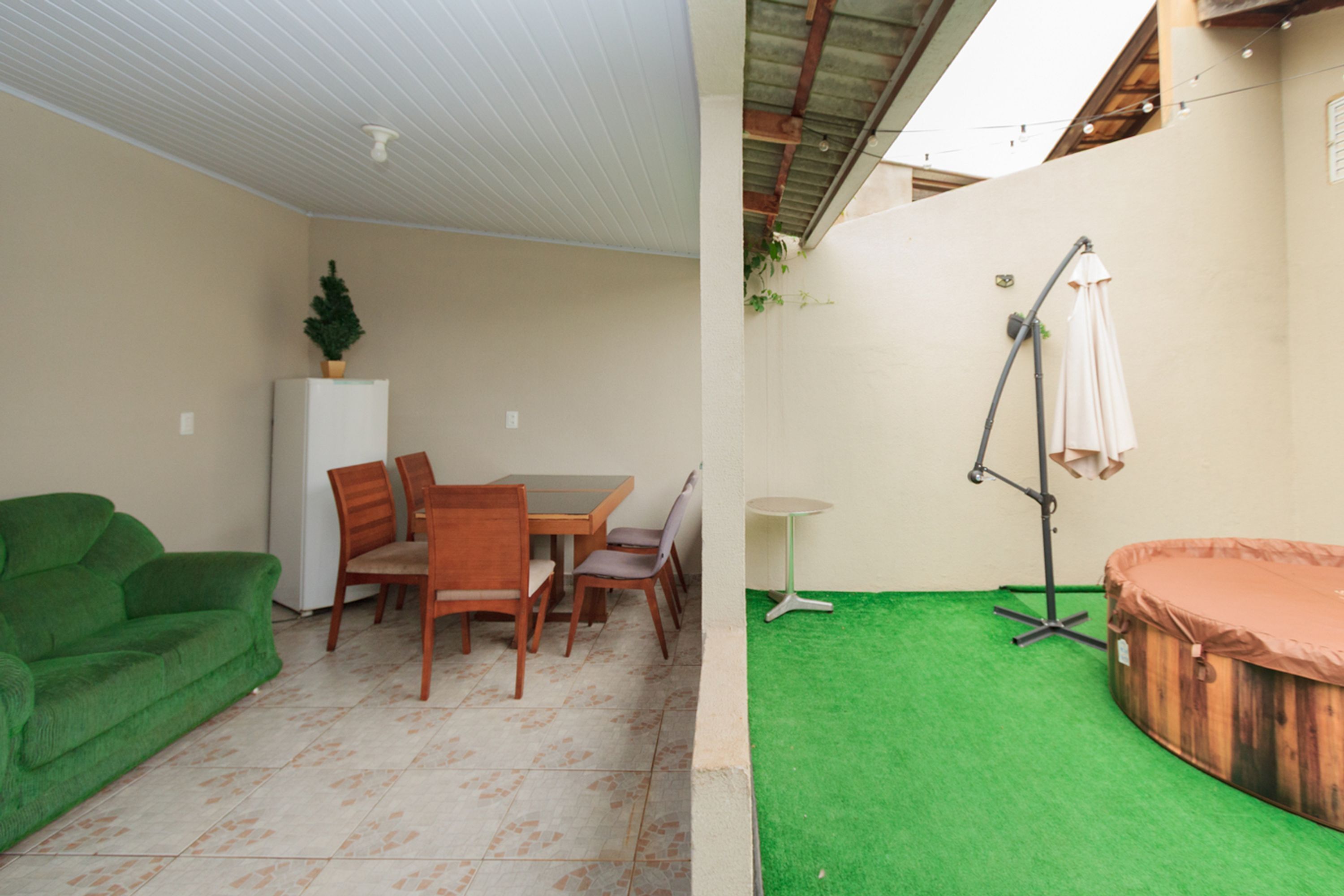 A room with a green couch, wooden chairs, a small table, a white cabinet, a green artificial turf area, and a wooden hot tub.