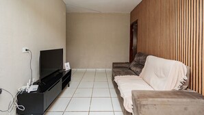 En stue med et fladskærms-tv på et sort stativ, en beige sofa og en væg beklædt med træpaneler.