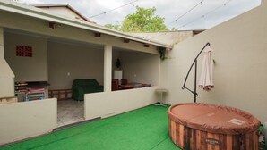 En overdækket terrasse med jacuzzi, et lille bord og en stol.