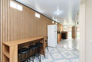 Une cuisine avec un mur en bois, un réfrigérateur blanc, une table en bois avec des chaises et un sol carrelé.