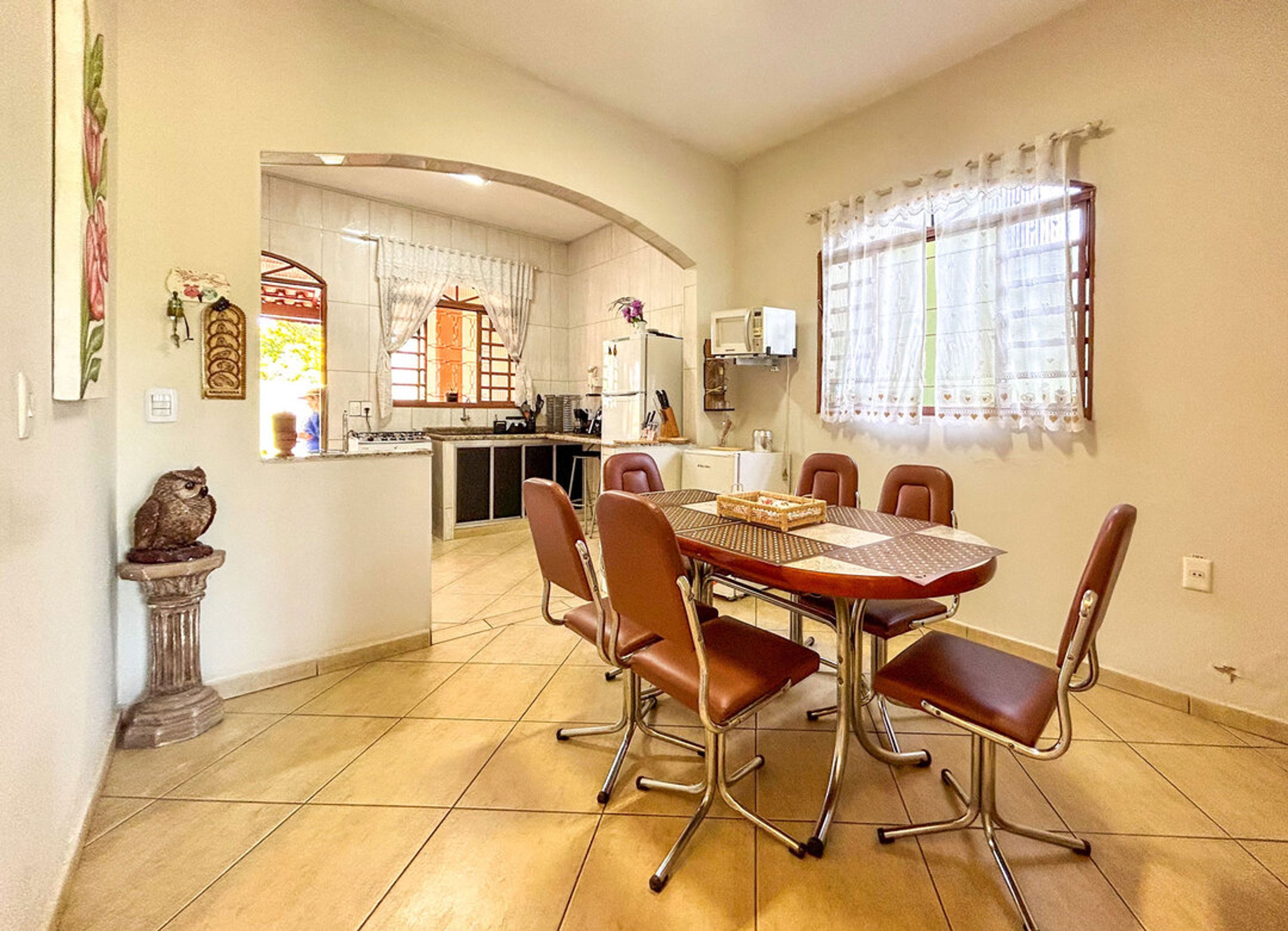 A dining area with a round table and six chairs, a kitchen in the background, and a decorative owl statue.