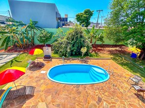 A swimming pool with a stone deck, surrounded by greenery and a few umbrellas.