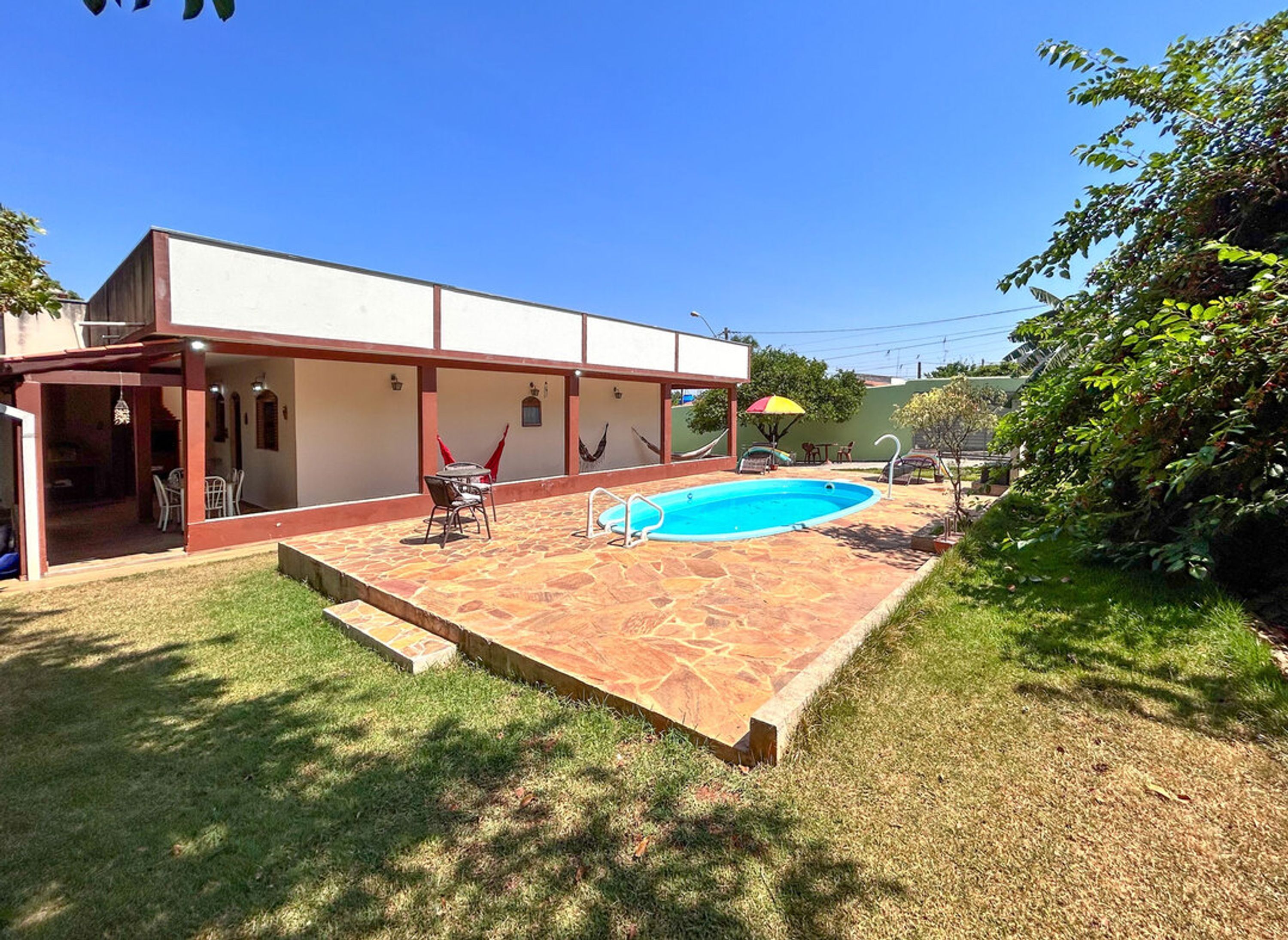 A backyard with a swimming pool, a covered patio area, and a grassy lawn.