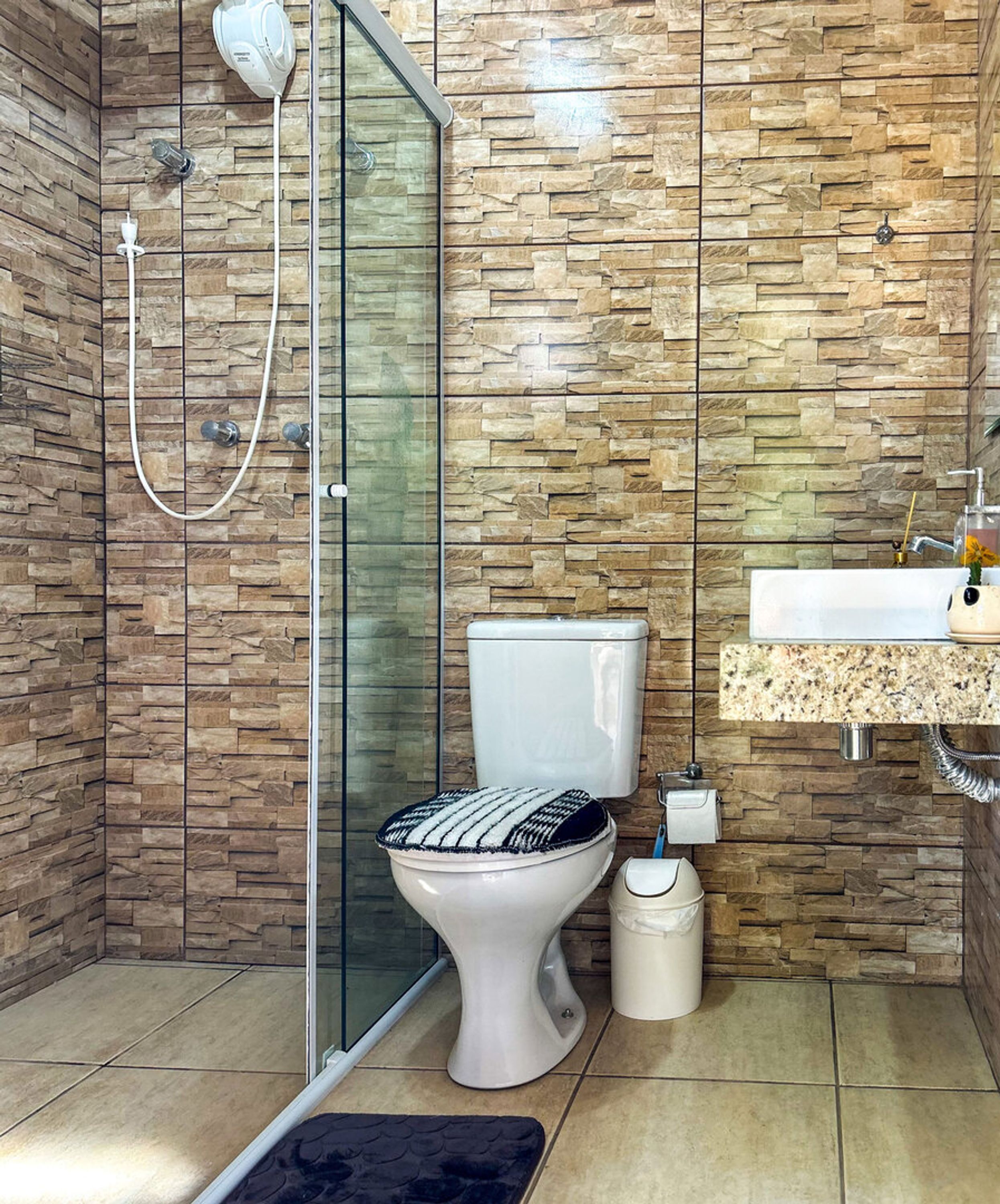 Un baño moderno con cabina de ducha de vidrio, un inodoro con asiento estampado y un lavamanos con encimera de mármol.