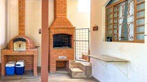 Horno de ladrillo al aire libre con una ventana, un escalón pequeño que lleva hacia él y dos contenedores azules en el suelo.
