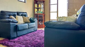 Una sala de estar con un sofá de cuero negro, un tapete morado y un aparador de madera con cristalería.