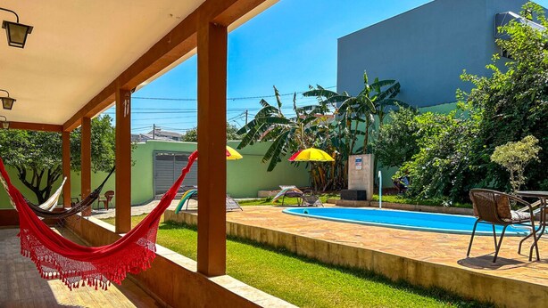 Un área de piscina con una hamaca, mobiliario exterior y vistas a un edificio al fondo.