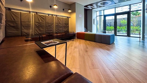 A modern waiting area with leather seating, a reception desk, and a large window with a view of greenery. - Timo Apto a 900m do Parque Ibirapuera com Wifi SP (São Paulo)