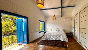 A bedroom with a large bed, a wooden floor, a blue door, and a view of greenery outside. - Casa pr x Praia de Santa Teresa Ilhabela SP (Ilhabela)