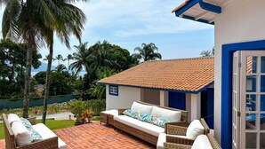 A patio with wicker furniture, a white sofa, and a blue door. - Casa pr x Praia de Santa Teresa Ilhabela SP (Ilhabela)