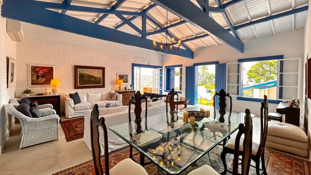 A spacious living room with a glass coffee table, comfortable seating, and a high ceiling with exposed beams. - Casa pr x Praia de Santa Teresa Ilhabela SP (Ilhabela)