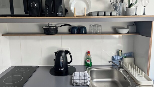 Eine moderne Küche mit Einbauherd, Wasserkocher, Spüle mit Geschirrständer und verschiedenen Küchenutensilien in den Regalen.