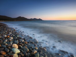 Une plage de galets bordée par une mer calme et dominée par des montagnes lointaines.