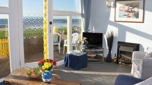 A living room with a TV, a fireplace, and a view of the beach through large glass doors.