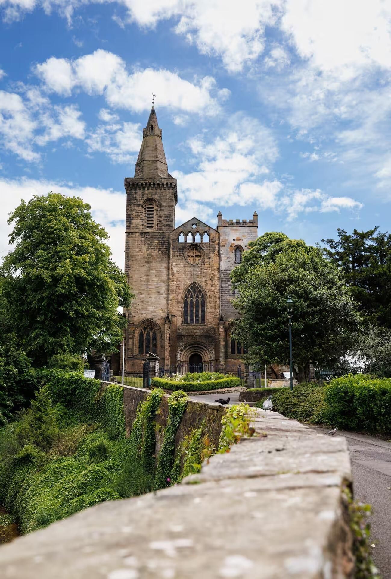 A historic church with a prominent tower and arched windows, surrounded by lush greenery and a stone pathway leading to the entrance.