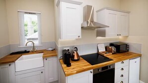 Cocina compacta con armarios blancos, encimera de madera, pileta, hervidor, tostadora y microondas.