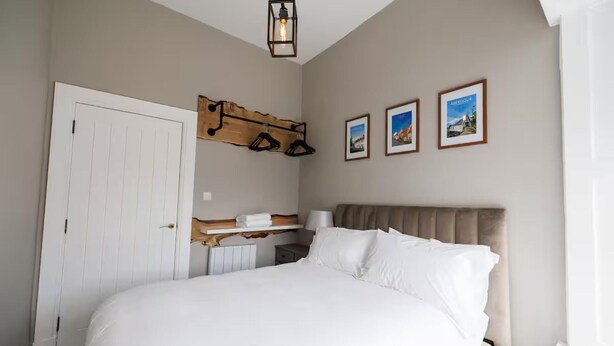 Une chambre à coucher avec un grand lit, une étagère en bois au-dessus du lit, une table de chevet et trois tableaux encadrés accrochés au mur.