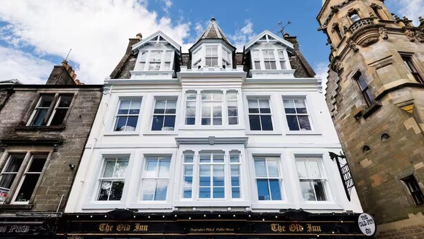 Un edificio histórico con una torre destacada y un cartel que indica "The Old Inn" a nivel de la calle.