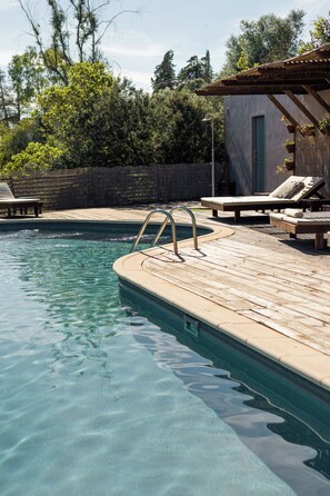 A clear swimming pool with a wooden deck, lounge chairs, and a small building with a green door. - Hotel Vale Do Gaio (Alcacer do Sal)