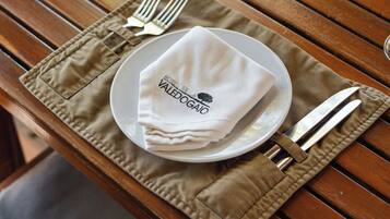 A wooden dining table set with a plate, napkin, fork, knife, and glass.