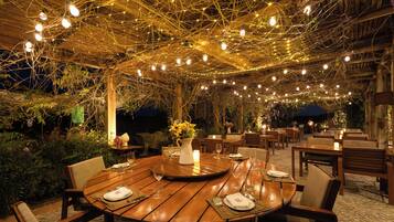 An outdoor dining area with wooden tables and chairs, string lights overhead, and a rustic ambiance.