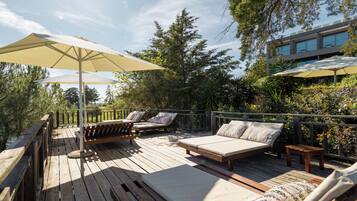 Una terraza de madera con mobiliario exterior, incluyendo un sofá y sillas, y dos sombrillas que dan sombra.