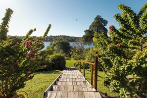 Una terraza de madera que da a un lago rodeado de exuberante vegetación y flores rosadas.