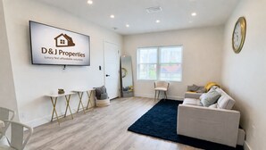 A modern living room with a sofa, a coffee table, and a rug. There is a television mounted on the wall displaying a logo. - Daytona Double Delight (Daytona Beach)