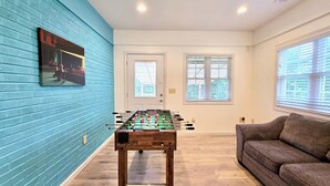 A room with a foosball table, a sofa, and a window with blinds. - Tranquil Ranch Style Retreat w/ 2+ Acres of Land (Marietta)