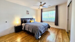 A bedroom with a bed, a ceiling fan, a window with blinds, and a nightstand with a lamp. - Tranquil Ranch Style Retreat w/ 2+ Acres of Land (Marietta)