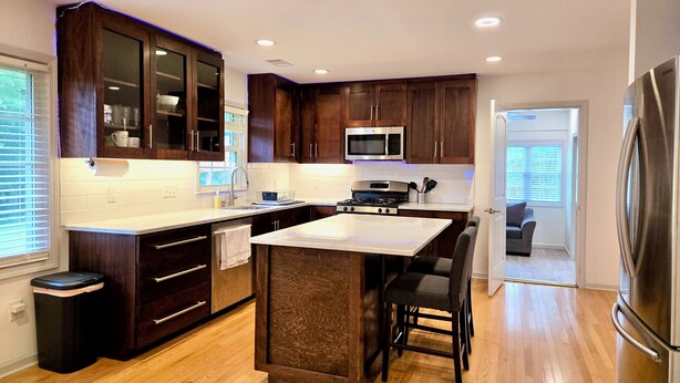 A modern kitchen with dark wood cabinets, a stainless steel refrigerator, a microwave, and a large island with bar stools. - Tranquil Ranch Style Retreat w/ 2+ Acres of Land (Marietta)
